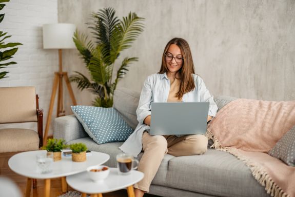 Junge Frau lächelnd am Laptop auf Sofa